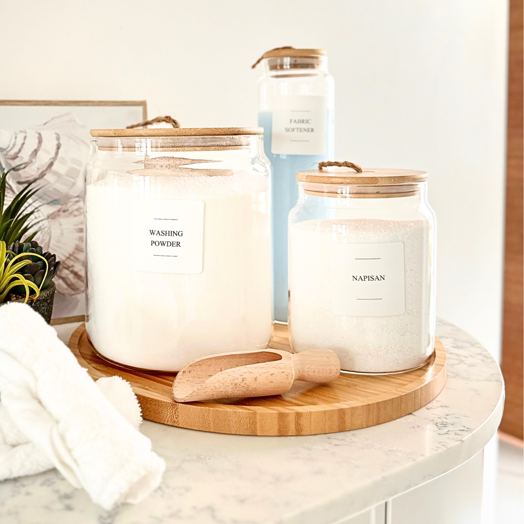 Candle and towels on a marble surface with a plant and framed picture in the background