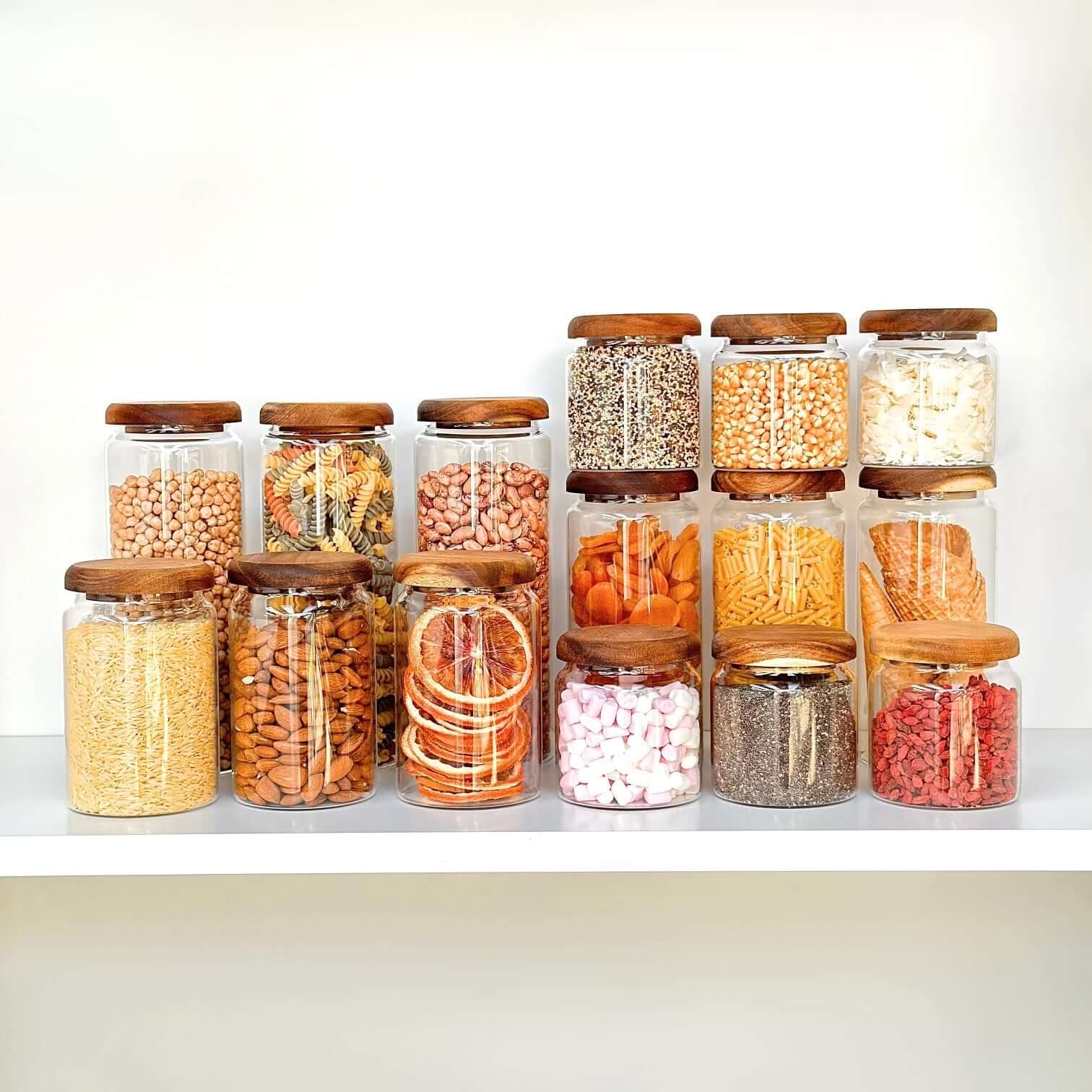 Glass jars with acacia lids filled with dry goods for kitchen pantry organization.