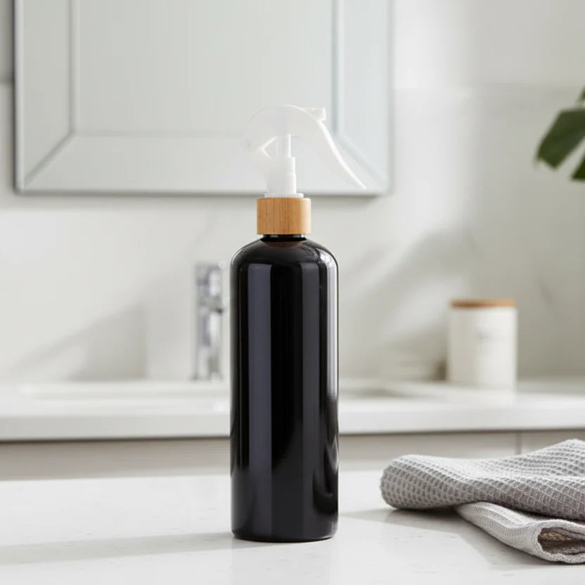 Black spray bottle with wooden cap on a light surface with plants in the background