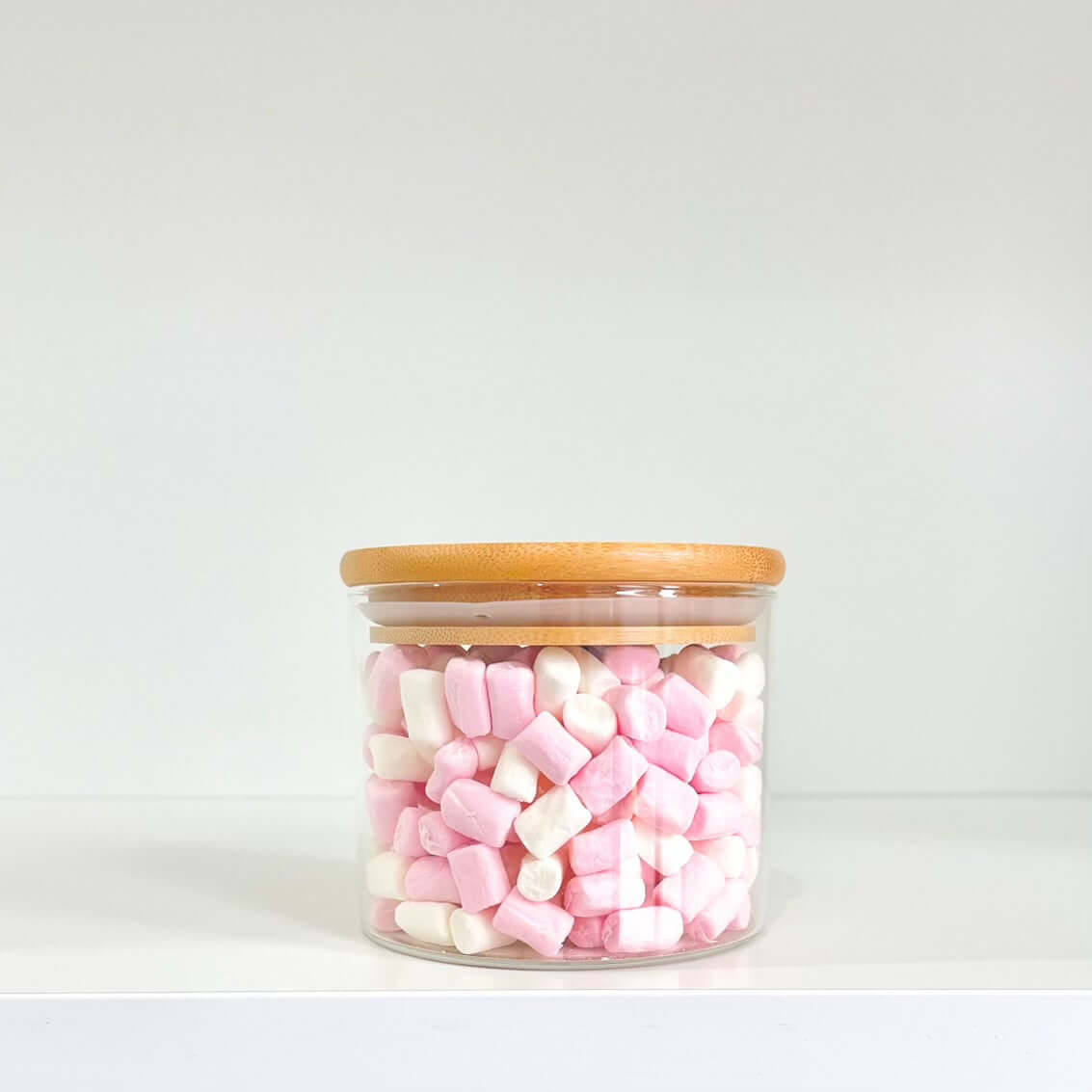 Bamboo glass jar with wooden lid storing pink marshmallows, perfect for pantry organization.